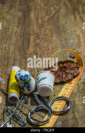 Bobine di filo di base e strumenti di cucitura tra cui i perni, un ago, un ditale e nastro di misurazione su un vecchio tavolo di legno. Foto Stock