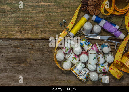 Bobine di filo di base e strumenti di cucitura tra cui i perni, un ago, un ditale e nastro di misurazione su un vecchio tavolo in legno. concetto con copia spazio. Foto Stock