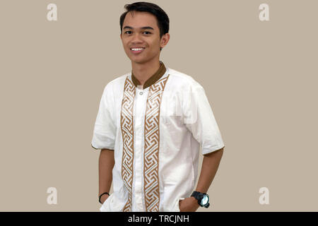 Ritratto di bello la gioventù musulmana sorridente ponendo di fronte alla telecamera. Isolato in sfondo marrone Foto Stock