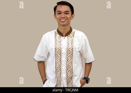 Ritratto di bello la gioventù musulmana sorridente ponendo di fronte alla telecamera. Isolato in sfondo marrone Foto Stock