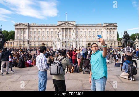 I turisti tenendo selfies e fotografie fuori Buckingham Palace, London, England, Regno Unito Foto Stock