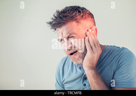 Di sesso maschile di dolore alle orecchie di toccare la sua dolorosa testa isolata su sfondo grigio Foto Stock