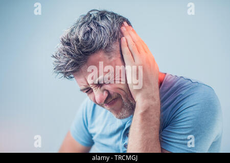Di sesso maschile di dolore alle orecchie di toccare la sua dolorosa testa isolata su sfondo grigio Foto Stock