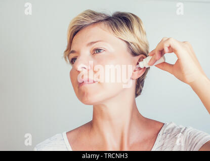 Donna che utilizza gocce auricolari su sfondo grigio Foto Stock