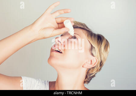 Una donna che fa uso di gocce per gli occhi in occhi Foto Stock