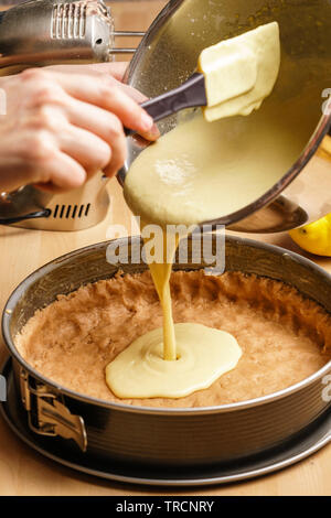 Due femmina mani caucasica pour cheesecake crema in un nero teglia, utensili da forno in background - Vista laterale, orientamento verticale Foto Stock