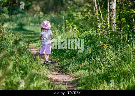 Vista posteriore dei giovani 3 anno vecchia ragazza con una bottiglia d'acqua in mano a camminare su uno stretto sentiero nel verde foresta estate Foto Stock