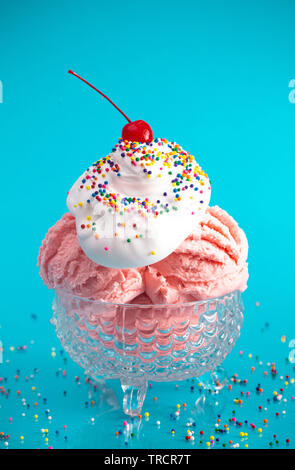 Un gelato alla fragola gelato su un brillante sfondo blu con una ciliegia sulla parte superiore Foto Stock
