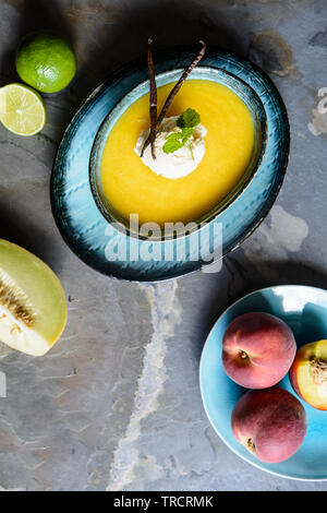 Estivo rinfrescante zuppa di frutta con Melone Galia e pesche, guarnita con una pallina di gelato alla vaniglia Foto Stock