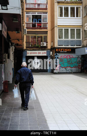 Il vecchio uomo con sacchetti di generi alimentari a piedi verso il suo appartamento Complex building in Granada, Spagna. Vecchiaia e solitudine, abbandono, indipendenza. Foto Stock