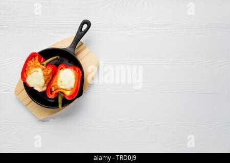 Il peperone ripiene di carne con formaggio fuso mozzarella in cima cotta al forno in padella in ghisa. Vista dall'alto. In legno naturale dello sfondo. Foto Stock