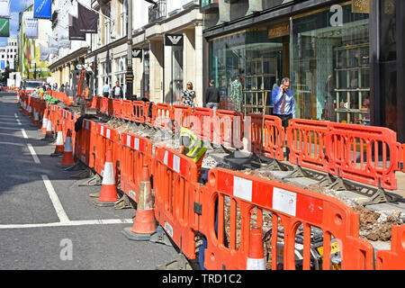Rosso barriera di plastica & coni che racchiude opere stradali per il contraente e i lavoratori in via cavo di scavo in trincea di strade e vie di Londra West End England Regno Unito Foto Stock