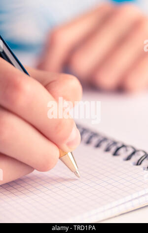 Teen scrive nero giallo penna in un notebook a scacchi. Compiti e piano giornaliero Foto Stock