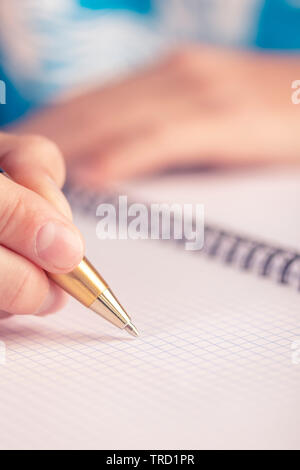 Teen scrive nero giallo penna in un notebook a scacchi. Esame a scuola Foto Stock