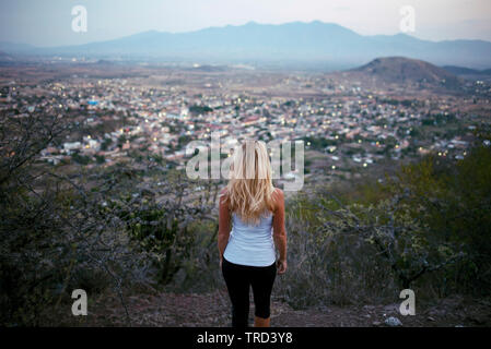 Donna bionda da dietro cercando di visualizzare in piedi sopra la città. Teotitlan del Valle, Stato di Oaxaca, Messico. Maggio 2019 Foto Stock