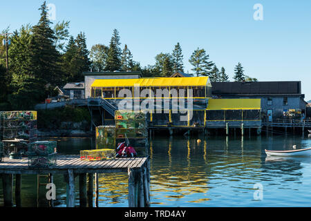 Una vista da cartolina porto basso Maine con un molo di aragosta trappole Thurstons lobster pound ristorante con tetto di colore giallo e una piccola barca a remi mored in t Foto Stock