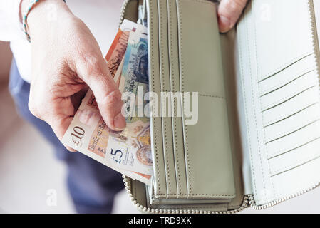 Stretta di mano di donna tenendo fuori di sterline dalla sua borsa Foto Stock