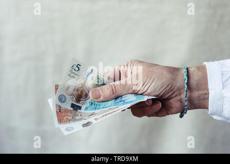 Stretta di mano di donna holding pounds sterlings Foto Stock