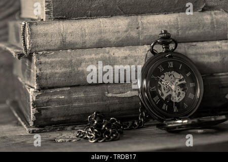 Antique telecomando tascabile guarda con una catena appoggiata su una pila di libri antichi. Su uno sfondo di legno con colori di tonificazione. Foto Stock