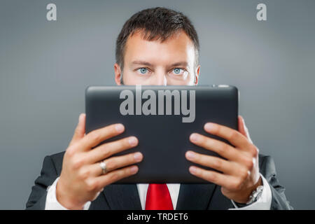 Ritratto di un simpatico imprenditore in un vestito nero tenendo un tablet nelle sue mani contro lo sfondo grigio Foto Stock