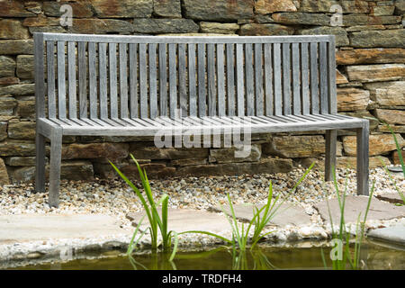 Svuotare panca in legno di fronte a un muro di pietra Foto Stock