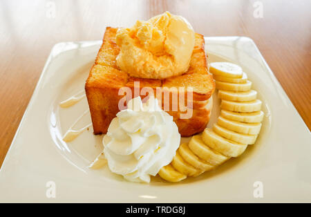 Pane dolce miele santos gelato alla vaniglia con panna montata banana di frutta e miele delle api su piastra bianca nella caffetteria cafe Foto Stock