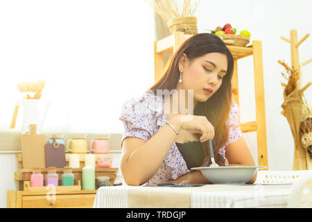 Lonely donna asiatica sedersi a tavola a mangiare pasti nella cucina da solo al mattino con la splendida luce del sole con spazio di copia Foto Stock