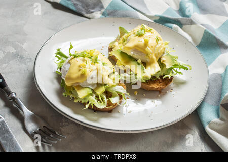 Uova Benedict con insalata e avocado su sfondo di calcestruzzo. Foto Stock