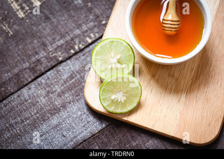 Il miele di lime sul bordo di taglio con il miele in coppa sul legno scuro dello sfondo Foto Stock