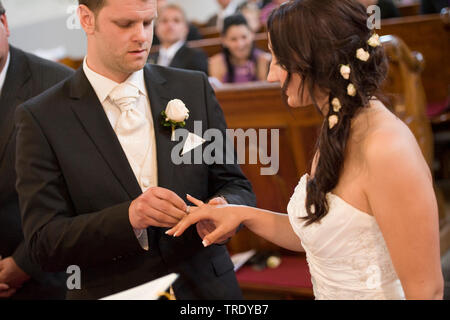 Lo sposo mettendo il matrimonio ad anello sulla sua sposa del dito durante la cerimonia di nozze Foto Stock