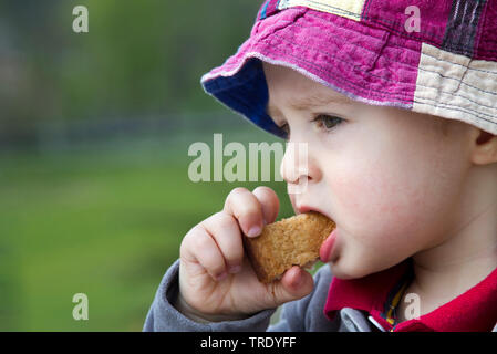 Testa-ritratto di spalla di un giovane ragazzo di mangiare all'aperto di un cookie Foto Stock