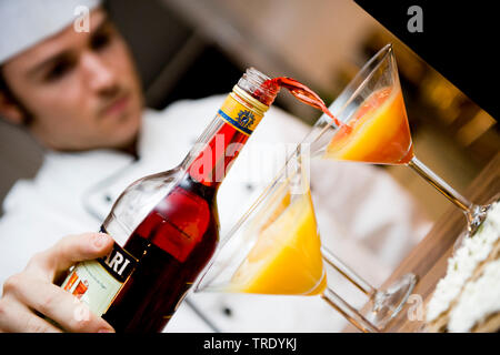 Cameriere riempie un bicchiere da cocktail di succo di arancia con Campari Foto Stock