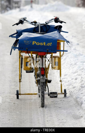 Portalettere's bike federale austriaco della posta su una coperta di neve road, Austria Foto Stock