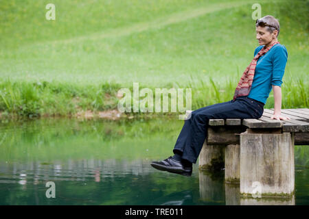 Ritratto di donna aelderly seduti sul pontile di un piccolo lago Foto Stock