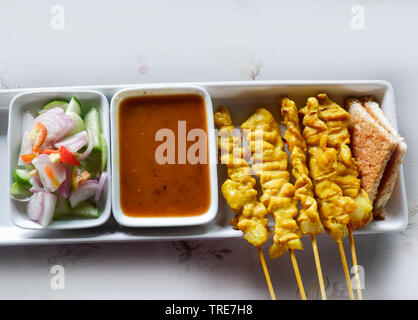 La carne di maiale satay con la tua salsa di arachidi / sottaceti che sono fette di cetriolo e cipolle in aceto Foto Stock