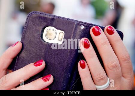 Donna con le mani di colore rosso chiodi in possesso di un telefono cellulare dotato di fotocamera digitale Foto Stock