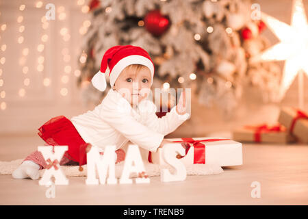 Bambina di 1 anno indossando santa clau suit strisciando su albero di Natale con le luci. Tempo di vacanza. Infanzia. Foto Stock