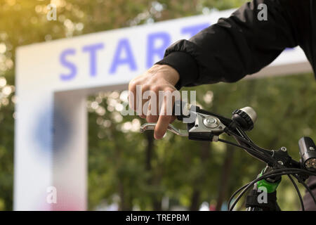 Ritagliato colpo di giovane uomo sulla bicicletta sul punto di inizio della corsa di ciclismo. Avviare il testo. Sfondo bokeh di fondo Foto Stock