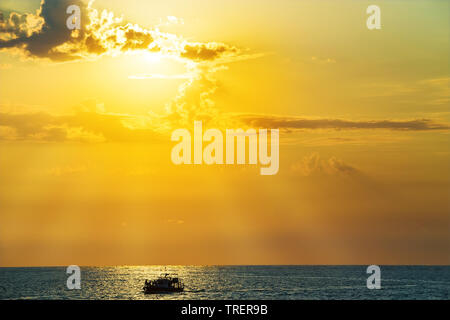 Barca con persone in mare al tramonto Foto Stock