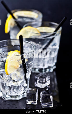 Tre Bicchieri con freddo fresca acqua gassata con le fette di limone e cubetti di ghiaccio closeup. Acqua di soda su sfondo nero. Foto Stock