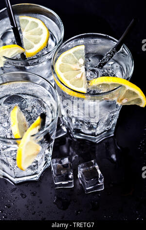 Tre Bicchieri con freddo fresca acqua gassata con le fette di limone e cubetti di ghiaccio closeup. Acqua di soda su sfondo nero. Foto Stock