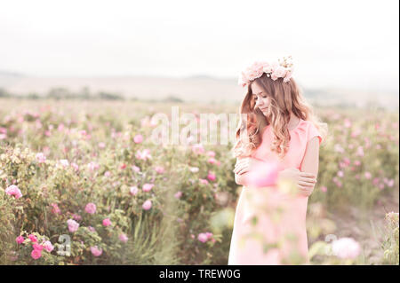 Teen ragazza 14-16 anni in posa nel giardino di rose. Indossare abiti eleganti e ghirlanda di fiori all'esterno. Foto Stock