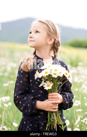 Carino kid girl 4-5 anni fiori di contenimento all'esterno. Guardando lontano. Durante la stagione estiva. Foto Stock