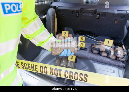 Funzionario di polizia tenendo un pacchetto di droga scoperto nel bagagliaio di una vettura Foto Stock