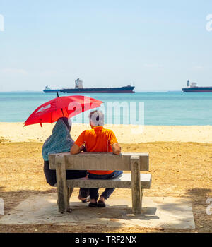 Giovane seduto su una panchina di cemento che guarda al mare East Coast Park di Singapore. Foto Stock