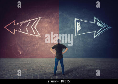Vista posteriore di dubbia l'uomo, le mani sui fianchi, di fronte a un muro di split come frecce andare in due modi diversi di rosso e di blu lato. La corretta scelta a sinistra o a destra Foto Stock