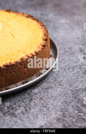 In casa gustosi piatti Vegan Cheesecake al limone su una piastra, grigio scuro dello sfondo di pietra - close-up, orientamento verticale copia spazio sulla destra Foto Stock