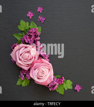 Composizione decorativa consistente di rose rosa, lilla viola fiori e foglie verdi su un nero ardesia con copy-spazio. Appartamento laico, vista dall'alto, overhead Foto Stock