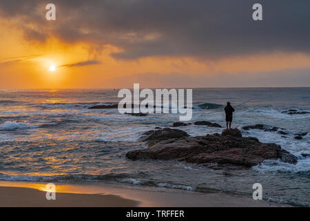 Pescatore solitario silhouette sulle rocce durante la bellissima alba. Durban, Costa Orientale, Sud Africa Foto Stock