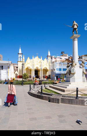 Donna locale indossando classic trecce peruviano camminando sul parco di Pino con la Chiesa di San Juan Bautista in background, Puno, Perù Foto Stock